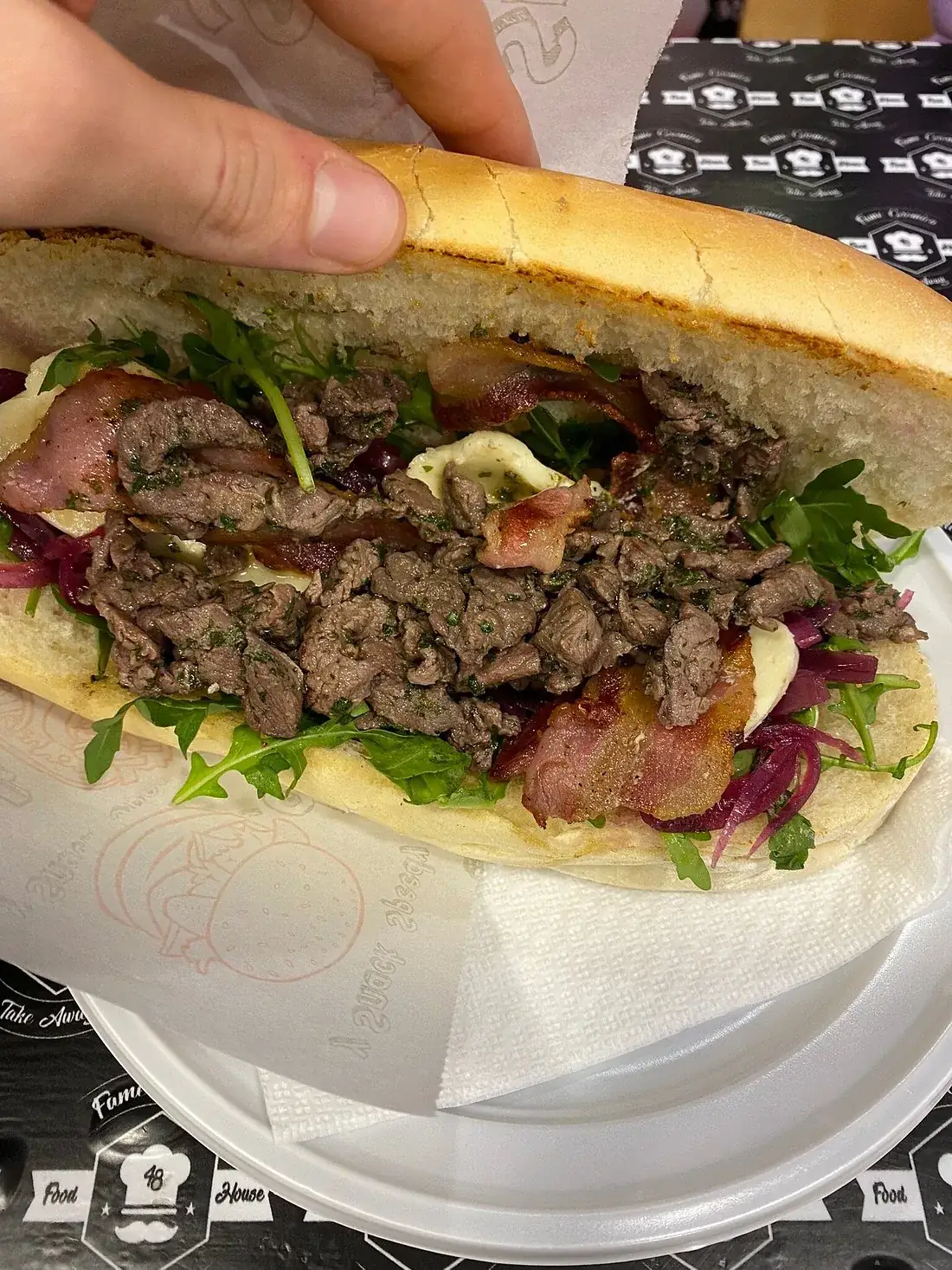 Caddozzone aperto con carne di cavallo tagliata al coltello, bacon, cipolla rossa, rucola e formaggio, servito su carta con il marchio Fame Cosmica