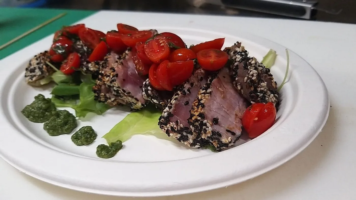 Piatto con tonno scottato in crosta di sesamo bianco e nero, pomodorini e pesto verde
